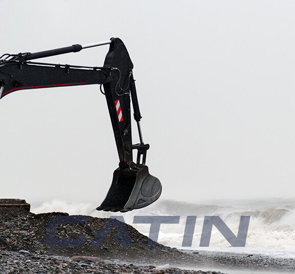 Excavator bucket scoops stones on the seashore in stormy weather.